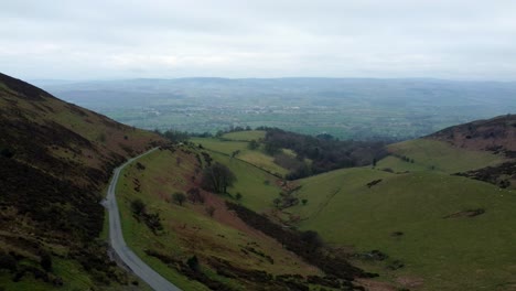Narrow-single-rural-road-running-through-Welsh-green-mountain-valleys-landscape-aerial-pull-back-left