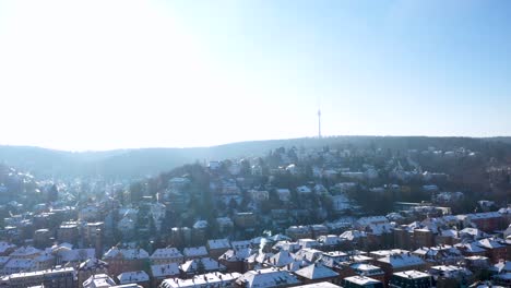 Aerial-top-down-view-tilting-up-revealing-beautiful-city-center-with-red-tile-roofs,-TV-Tower-and-mounatins-covered-in-snow-during-winter-in-Stuttgart,-Germany