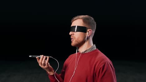 Ein-Angenehmer-Mann-Mit-Kopfhörern-Spricht-Mit-Geklebten-Augen-Per-Sprachnachricht-Auf-Einem-Smartphone