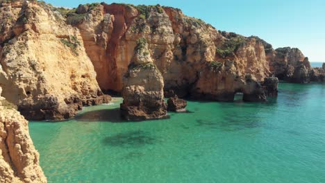 Craggy-cliffs-jutting-out-of-crystal-clear-waters-of-the-Algarve-Sea,-in-Lagos,-Portugal---Aerial-ground-level-Fly-over-shot