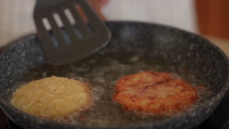 Close-up-of-frying-fresh-homemade-hashbrown-potato-puffs-in-oil-as-they-are-being-flipped-with-a-spatula