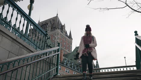 Girl-Walking-Down-The-Stairs-Near-Chateau-Frontenac-Hotel-At-Wintertime-In-Old-Quebec,-Quebec,-Canada