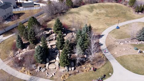 Drone-shot-flying-around-a-children’s-rock-park-and-playground-in-a-circle,-as-kids-play-together-on-a-sunny-spring-day-after-covid-19-lockdown-restrictions-are-lifted