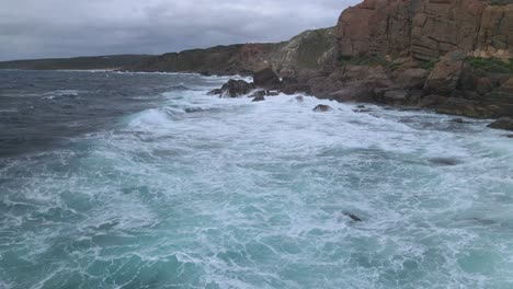 Flyover-strong-sea-waves-crashing-rocks-during-storm-in-cloudy-day-in-australian-beach