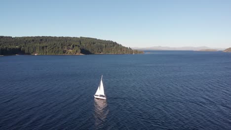 Aerial-flight-tracks-bright-white-sailboat-sailing-on-deep-blue-lake