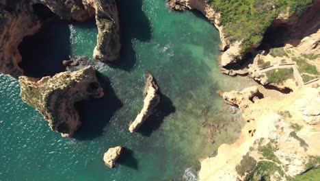 Birds-eye-view-over-Rugged-jagged-Algarve-Coastline,-In-Lagos,-Portugal---Aerial-Top-rotation-shot