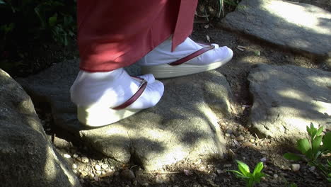 The-feet-of-Japanese-women-wearing-tabi-socks-and-geta-sandals-walk-on-stepping-stones-in-a-Japanese-garden