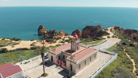 Red-Lighthouse-at-the-end-of-the-Ponta-da-Piedade-in-Lagos,-Algarve,-Portugal---Aerial-Orbit-Point-of-interest