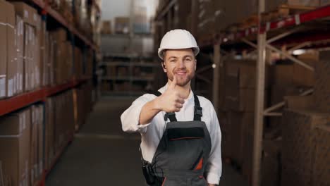 man-in-work-uniform-pointing-finger-up-at-camera-on-background-of-racks-with-boxes