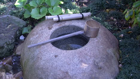 Una-Cuenca-De-Agua-De-Lluvia-Descansando-En-La-Parte-Superior,-En-Un-Jardín-De-Té-Japonés