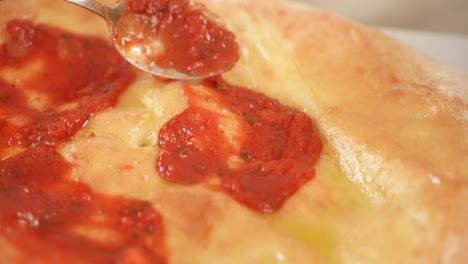 La-Mano-Usa-Una-Cuchara-De-Metal-Para-Aplicar-Salsa-De-Tomate-En-La-Masa-De-Pizza,-Cámara-Lenta
