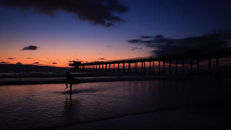 Silueta-De-Surfista-Caminando-En-La-Playa-En-La-Jolla,-San-Diego-Al-Atardecer