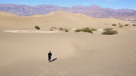 Western-caucasian-male-walking-alone-down-a-huge-sand-dune-in-the-desert