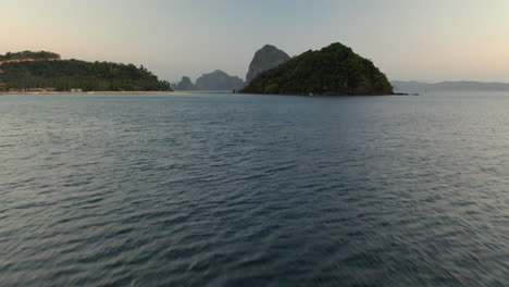 Aerial-flying-low-over-water-showing-Depeldet-Island-after-sunset,-El-Nido,-Palawan,-Philippines