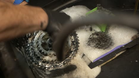 Male-bicycle-mechanic-scrubs-a-chainring-in-a-workshop-basin