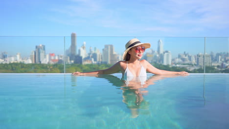 Rich-asian-woman-in-infinity-swimming-pool-on-sunny-day-with-urban-cityscape-in-background,-full-frame