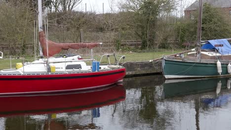Kleine-Rotgrüne-Segelboote,-Die-An-Einem-Schmalen-Ländlichen-Kanaljachthafen-Festgemacht-Sind