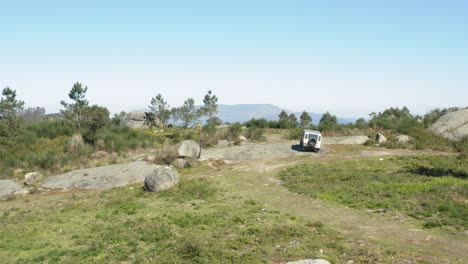 Off-road-vehicle-making-U-turn-on-top-of-Northern-Portuguese-mountain---Aerial-Ground-level-slide-tracking-shot