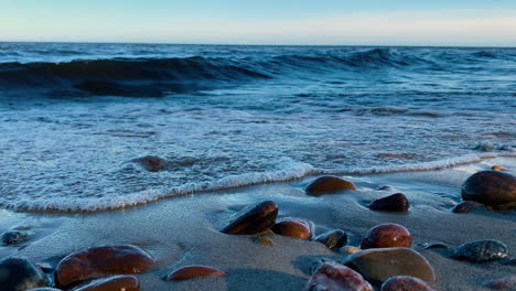 Waves-washing-up-on-sandy-beach-with-round-and-smooth-pebbles