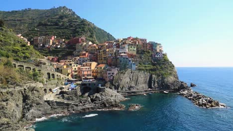 Static-view-overlooking-Manarola-coastline,-harbor-and-bay-with-colorful-small-town-houses-and-clear-water-on-a-sunny-summer-day-in-Cinque-Terre,-Liguria-Italy