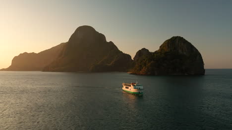 Aerial-showing-a-big-ferry-going-in-to-the-harbour-of-El-Nido-with-sunset,-Palawan,-Philippines