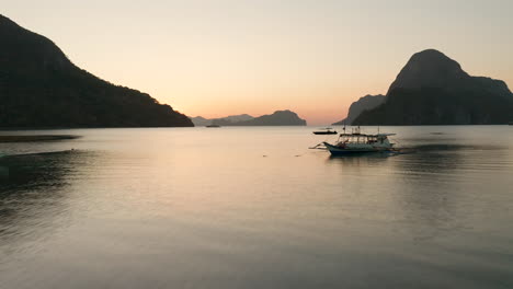 Aerial-showing-an-outrigger-boat-and-Cadlao-Island-with-sunset-and-golden-hour-in-El-Nido,-Palawan,-Philippines