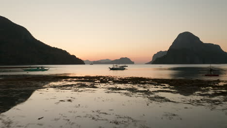 Aerial-flying-backwards-showing-outrigger-boat-with-sunset-and-golden-hour-in-El-Nido,-Palawan,-Philippines