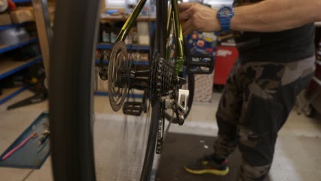 Male-bicycle-mechanic-turns-crank-and-adjusts-front-derailleur-whilst-on-workshop-stand