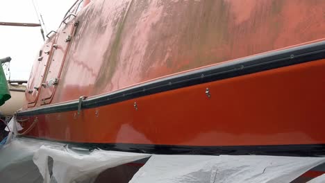 Disused-abandoned-orange-RNLI-lifeboat-survey-vessel-in-secure-fence-shipyard-pull-back-slow