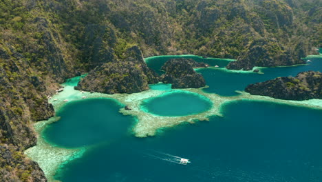 Aerial-shot-showing-an-outrigger-boat-near-a-deserted-tropical-island-of-El-Nido,-Palawan,-Philippines