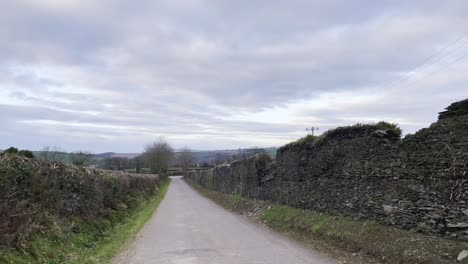 Static-footage-of-a-rural-road-in-Ireland-on-a-cloudy-afternoon-with-stonewall-on-sides