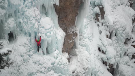 Ice-climber-with-axe-climbing-on-frozen-waterfall-in-cold-snowy-winter-landscape-wide-view
