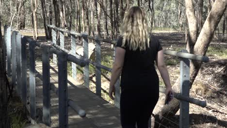 Outdoor-nature-blonde-pretty-woman-walking-along-bridge-in-nature