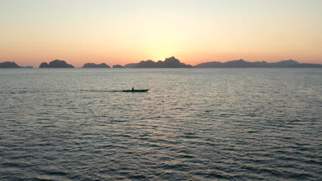 Aerial-showing-a-wooden-fishing-boat-crossing-with-the-sunset-in-the-background-in-El-Nido,-Palawan,-Pilippines