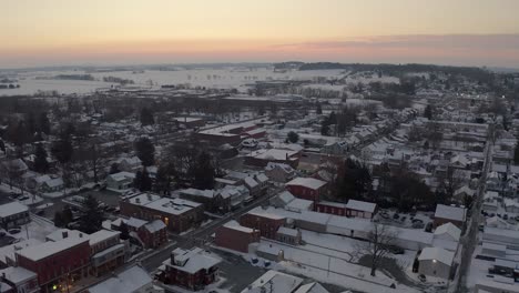 High-aerial-above-town-in-USA-covered-in-winter-snow-during-colorful-sunrise,-sunset