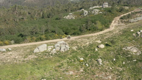 Mountain-Bikers-gliding-fast-down-a-dirt-road-in-Alto-Minho,-Portugal---Aerial-Wide-Orbit-Tracking-shot