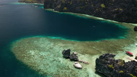 Aerial-tilting-down-on-tropical-water-by-Matinloc-Island,-El-Nido,-Palawan,-Pilippines
