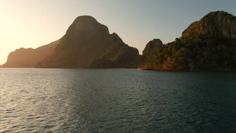 Aerial-flying-low-over-water-showing-Cadlao-Island-with-sunset-and-golden-hour-in-El-Nido,-Palawan,-Philippines