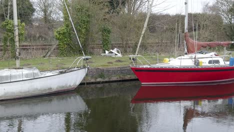 Small-grungy-sailboats-on-narrow-rural-countryside-canal-marina-dolly-right