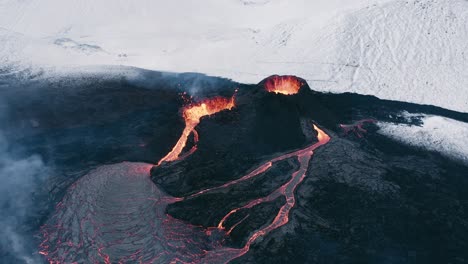 Erupting-volcano-in-remote-Iceland-landscape-with-snowy-mountains,-aerial