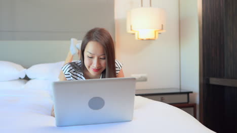 Mujer-Bastante-Asiática-Acostada-En-La-Cama-Mientras-Trabaja-En-Una-Computadora-Portátil