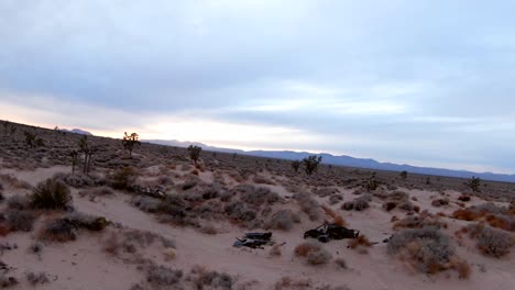 Ein-Verlassenes-Und-Ausgebranntes-Auto-Auf-Einem-Pfad-In-Der-Wildnis-Der-Mojave-Wüste---Luftumlaufansicht