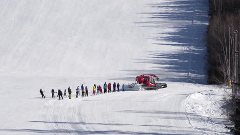 Roter-Pistenraupe,-Der-Rechts-Abbiegt-Und-Eine-Gruppe-Von-Skifahrern-Schleppt,-Schneebedeckter-Hügel