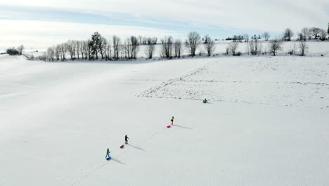 Aerial-Shot-Of-People-Walking-To-The-Top-Of-A-Snow-Covered-Ski-Hill-With-A-Sled,-Winter-Activity