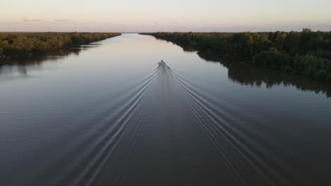 Aerial-shot-of-cruising-speed-boat-on-calm-amazon-river-moving-away-during-epic-sunset-at-background