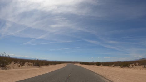 Driving-along-a-dusty-and-empty-road-in-the-middle-of-the-desert--driver-point-of-view