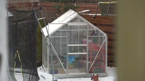 Small-glass-greenhouse-in-garden-during-snowfall.-Slow-Motion