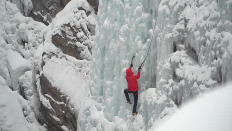 Ice-climber-climbing-on-frozen-waterfall-in-cold-white-winter-mountain-landscape