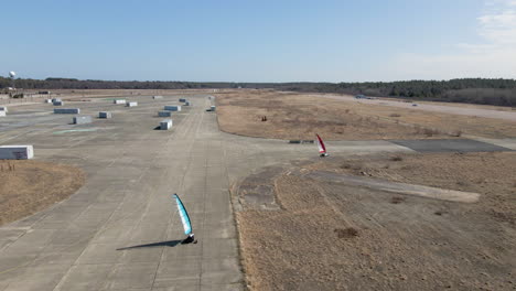 Aerial-Drone-tracking-shot-of-two-land-sailing-buggies-turning-a-corner-of-disused-airfield