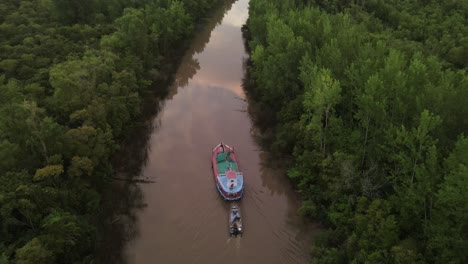 Filmische-Drohnenaufnahme-Eines-Schiffes-Mit-Kleinem-Boot-Auf-Dem-Amazonas,-Umgeben-Von-Grünen-Regenwaldbäumen-Bei-Sonnenaufgang